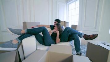 Joyful couple in love relaxing on a sofa surrounded by moving boxes video