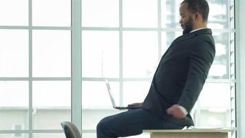 Exhausted young businessman straightens his shoulders while resting laptop video
