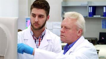 Senior scientist guides young intern on monitor in laboratory video