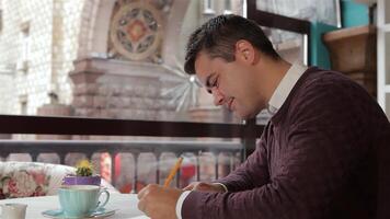 Thoughtful man writing in his notebook at a cozy cafe video