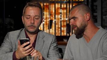 Mature men sharing a laugh over whiskey while exploring a smartphone video
