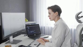 Charming young woman smiling at the camera while multitasking on two computers video