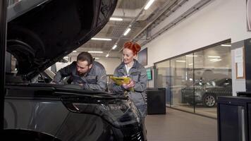 Dedicated car mechanics inspecting engine while taking notes video