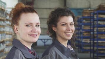 Confident female engineers beaming at the camera in a bustling factory video