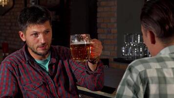 Mature bearded man savoring beer while engaging in conversation with a friend at the pub video