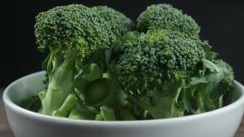 Fresh green broccoli in bowl rotating against black background. market display video