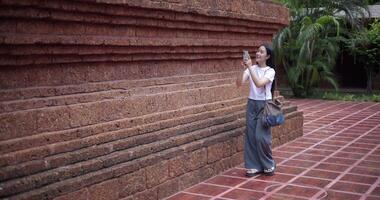 Handheld shot, Solo female tourist enjoying takes photos with mobile phone while strolling around, admiring the peaceful atmosphere and cultural beauty of the place. video