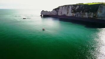 Fishing boat at rocky shores in the sun. White fishing boat off the coast of France against the backdrop of high cliffs of Etreta. video