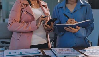 Two women standing at a desk with a notebook and pen photo
