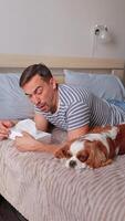 Dog is sleeping and in the background man is suffering from allergy to pet hair and is using tissues and medicine. He is sitting next to dog on bed. Health concept video