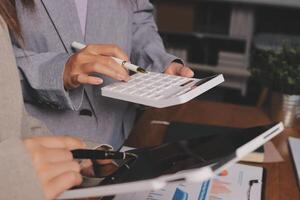 Two people are using a calculator and pen to write on a tablet photo