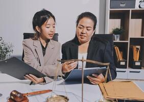 Two businesswomen in suits sitting at a desk with a tablet and a scale photo