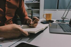 Man writing in notebook at desk with laptop and coffee mug photo