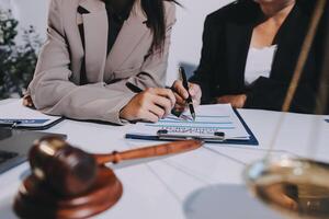Two businesswomen are writing on a document while a gavel is in the background photo