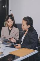 Two asian women in business attire sitting at a table with a laptop photo