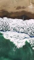 Aerial view capturing emerald green waves breaking over golden sand, white foam cascading along pristine coastal landscape with serene marine scenery video