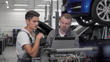 Two auto mechanics collaborating on car diagnostics with a laptop in the garage video