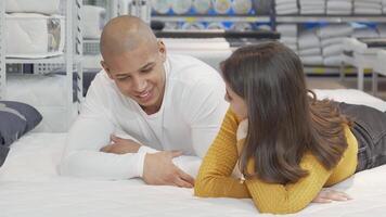 Young couple enjoying a playful conversation while lounging on a cozy bed in a furniture store video