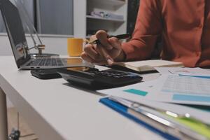A person is working on a calculator at a desk photo