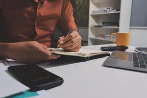 Man writing in notebook at desk with laptop and notebook photo