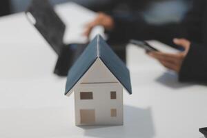 A house model is sitting on a table with a laptop and a person using a cellphone photo