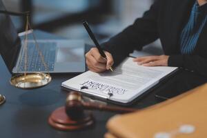 A lawyer writing on a legal document in front of a laptop and a gavel photo