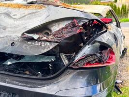 Rear view of a burned car with melted taillights, shattered glass, scorched paint, and extensive fire damage exposing internal components and wiring photo