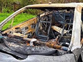 Side view of a completely destroyed car cabin with burnt seats, exposed metal frames, rusted steering column, and ash-covered interior after a severe fire photo
