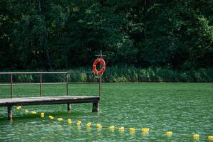 Serene lakeside scene with wooden dock and life buoy in summer. Weekend concept near the forest and lake photo