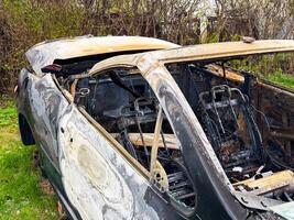 Burned car roof and cabin frame showing heat-warped metal, missing windows, and exposed seat structures after complete fire destruction of the upper body and interior photo