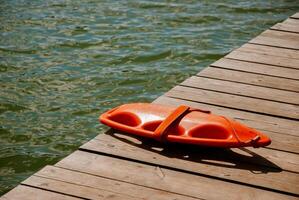 Lifeguard rescue float on wooden dock by lake water surface in summer. Weekend concept near the forest and lake photo