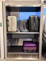 A train luggage rack with multiple modern suitcases in various colors and sizes, neatly organized on two metallic shelves during a daytime journey photo