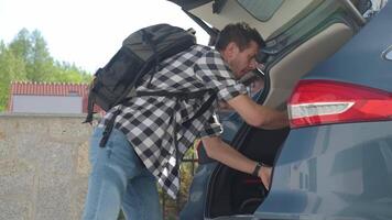 Man loading orange suitcase into car trunk. Packing luggage for travel video