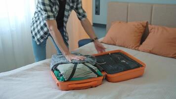 Man trying to close over packed orange suitcase before trip. Male traveler has trouble while packing a lot of clothes, preparing for travel video