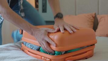 Man trying to close over packed orange suitcase before trip video