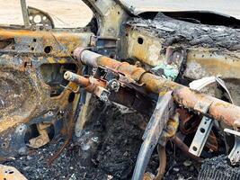 Burned steering column and dashboard frame from a car showing rusted metal structure, melted components, and complete fire destruction of the interior photo