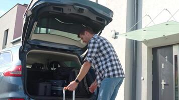 Man loading orange suitcase into car trunk before journey. Packing luggage for travel video
