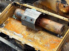 Burned steering column lock from a car with heavy rust and fire damage, showing the metal locking mechanism and oxidized surface inside a charred dashboard frame photo