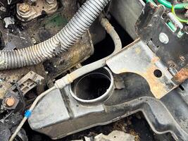 Car radiator neck and mounting bracket showing exposed coolant inlet, rusted metal support, and surrounding engine bay components after fire and mechanical damage photo