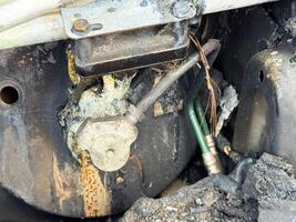 Burned air conditioning compressor valve from a car showing heat damage, melted sealing material, exposed copper wiring, and connected refrigerant lines photo