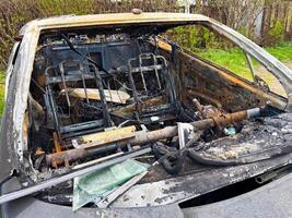 Interior of a completely burned car showing rusted metal frames, charred dashboard, melted components and exposed wires after an intense fire incident photo