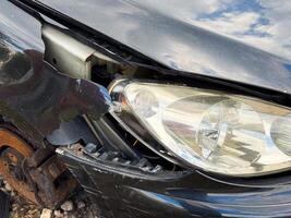 Broken front fender and headlight from a car showing cracked plastic panel, exposed structural frame, and intact headlamp with surrounding fire and collision damage photo