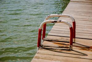 Calm lakeside scene with wooden dock and rusted metal ladder for relaxation and recreation. Weekend concept near the forest and lake photo