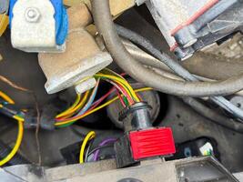 Close-up of a car engine wiring connector with red locking tab and multicolored wires, part of the vehicle's electrical harness located in the engine compartment photo