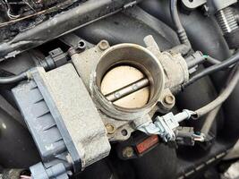 Close-up of a car engine throttle body showing the butterfly valve, electronic actuator, and surrounding connectors, part of the air intake and control system photo