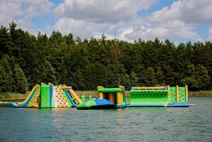 Inflatable obstacle course on lake with forest backdrop for summer fun. Weekend concept near the forest and lake photo