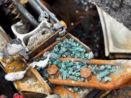 Close-up of shattered automotive safety glass scattered over a burned and rusted metal car seat frame, with visible melted elements and fire damage photo