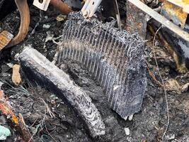 Burned heater core from a car showing severe fire damage, melted fins, and exposed internal structure lying among charred debris and wiring remnants photo