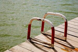 Tranquil lakeside summer scene with wooden dock and water access ladder. Weekend concept near the forest and lake photo