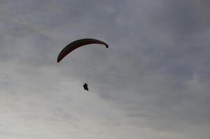 A man flying on a paraglider or gliding parachute. Silhouette of a flying man against the sky, view from below photo